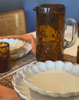Brown ceramic pitcher on a table with white ceramic plates and a woven basket.