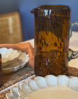 Brown ceramic pitcher on a table with white ceramic plates and a woven basket.