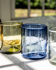 Four glass tumblers on a windowsill with a blurred outdoor background