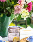 Floral arrangement in a green vase on a table with a glass of water and lemon.