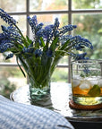 A small clear sculptured glass vase filled with flowers beside a clear drinking glass