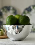 Green limes in a silver bowl with a blurred background