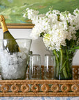 Bottle of champagne with ice, glasses, and a vase of white flowers on a decorative tray.