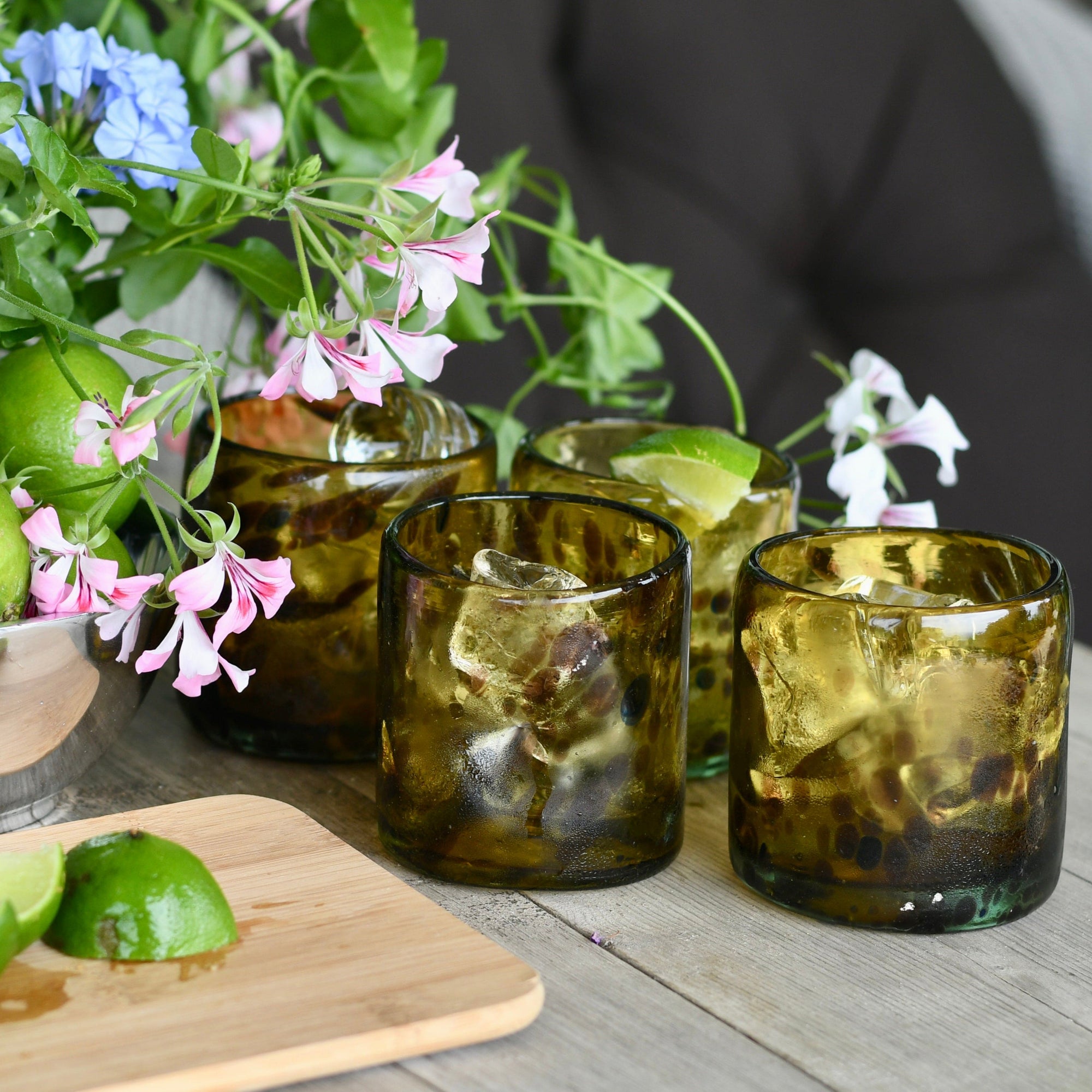 Brown glasses with ice and lime wedges on a wooden table with flowers in the background.