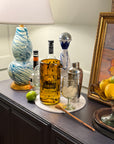 Decorative items including a bottle, glass, and fruit on a table with a painting in the background.