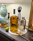 Decorative items including a bottle, glass, and fruit on a table with a painting in the background.