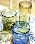 Blue glass with a lime wedge on a woven coaster, surrounded by green glasses on a decorative tray.