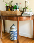 Wooden console table with decorative items including bottles, a vase, and books in a room with a window.
