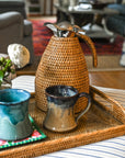 Wicker tray with mugs and decorative items on a striped sofa in a living room.