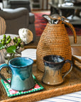 Wicker tray with mugs and decorative items on a striped sofa in a living room.