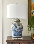 Decorative lamp with blue floral patterns on a wooden table next to a window and a painting.