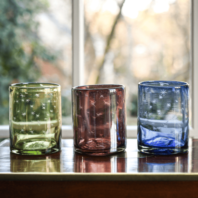 Four colorful glass tumblers on a reflective surface with a blurred natural background