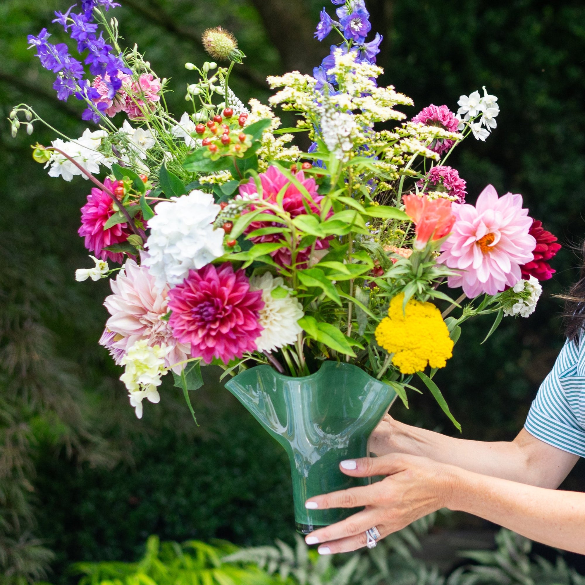 A colorful floral arrangement in a clear, fluted glass vase held by a person.
