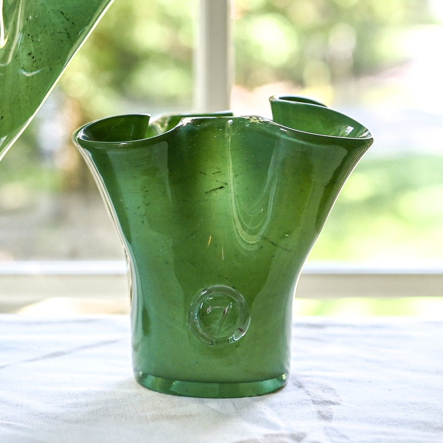 A handcrafted green glass vase with a lettuces leaf design on a table, with a blurred background.
