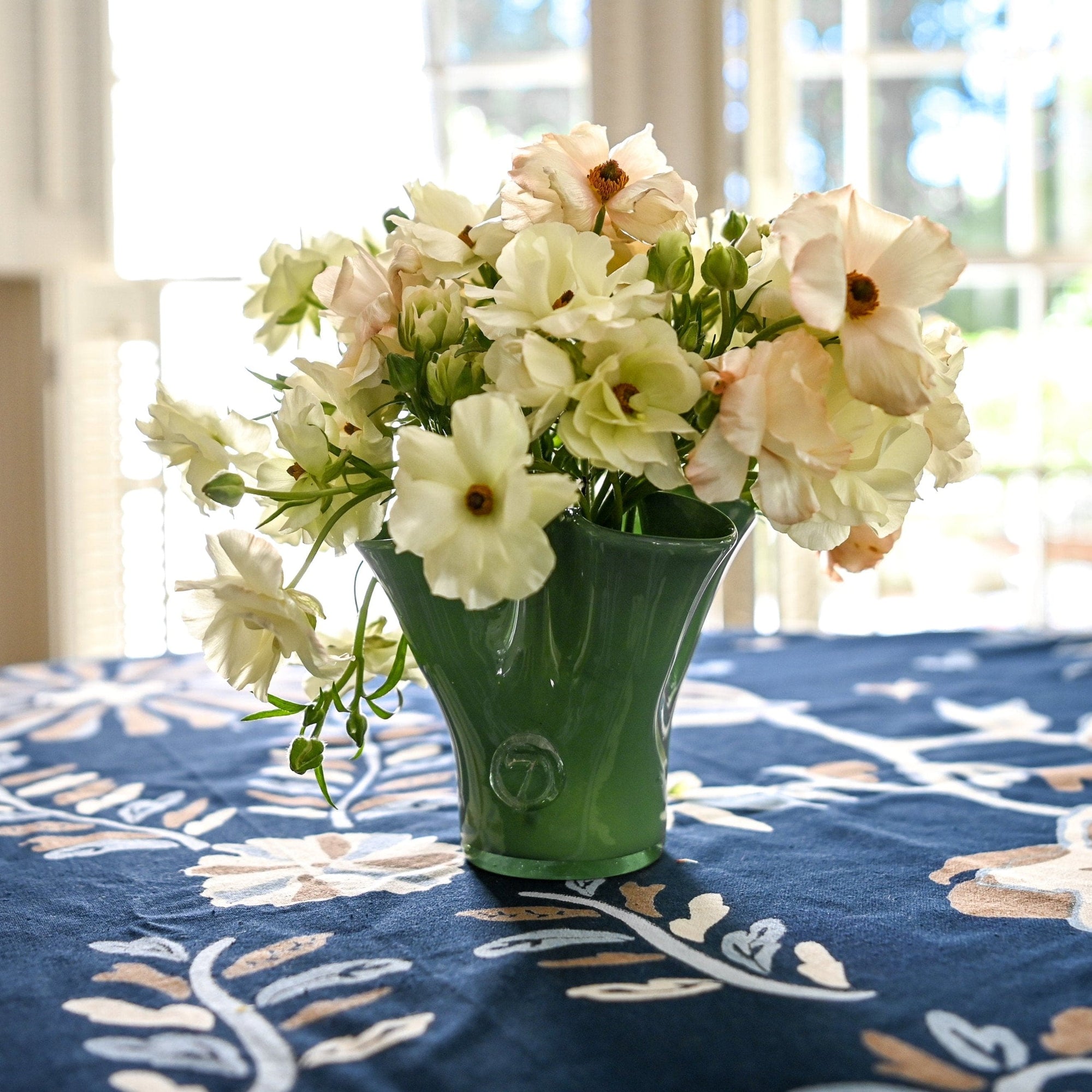 A petite green glass vase with flowers on a table