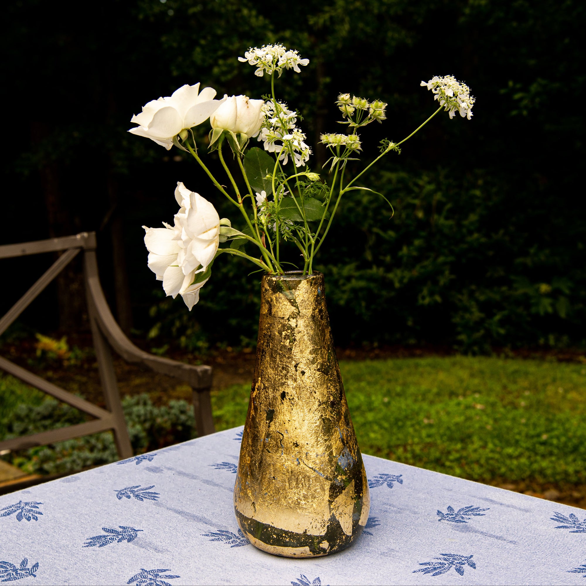 Decorative vase on 14k gold leaf with white flowers on a table outdoors