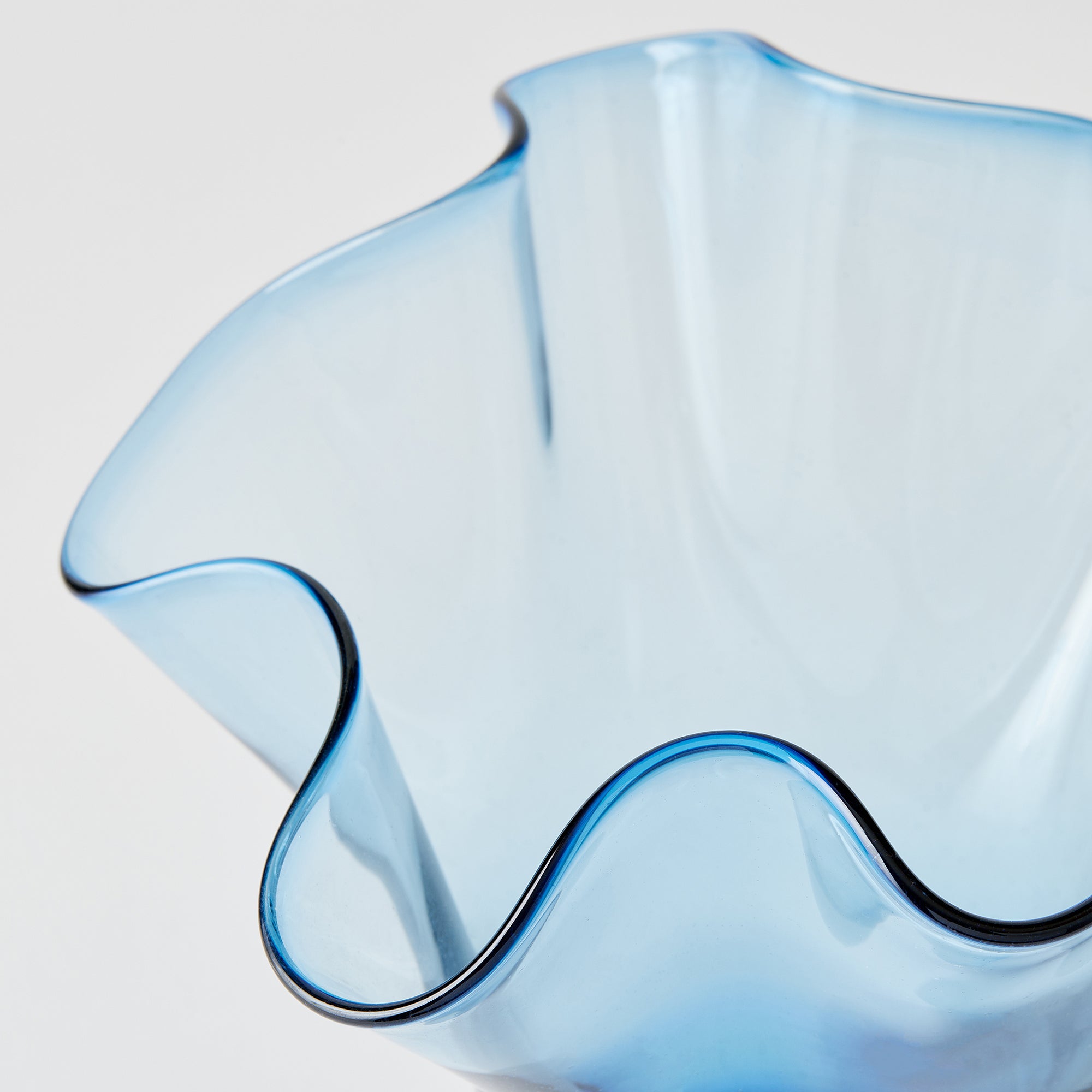 Blue glass vase with wavy edge on a light gray background