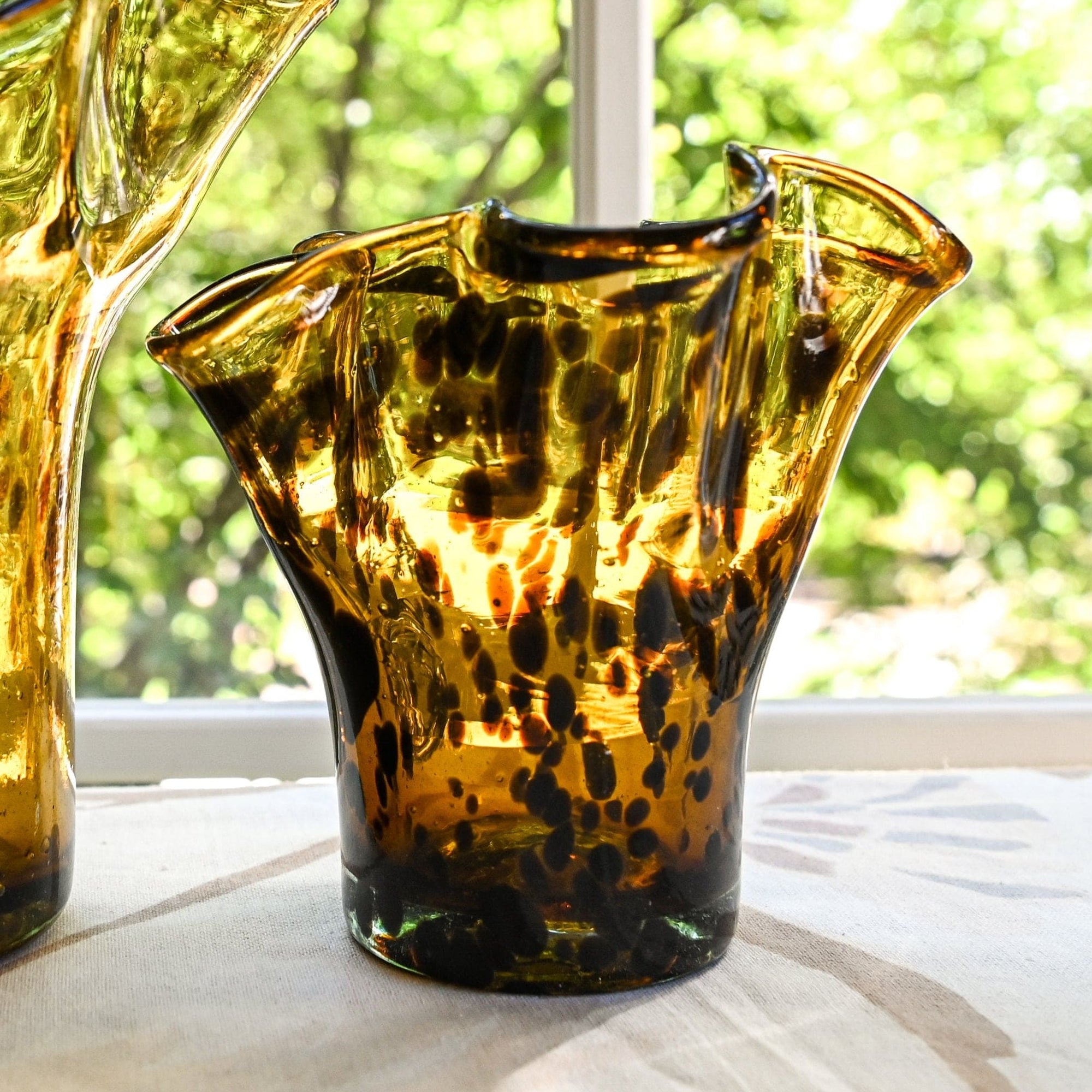 A handcrafted brown glass vase with a lettuce leaf design, sitting on a white surface with a blurred background.