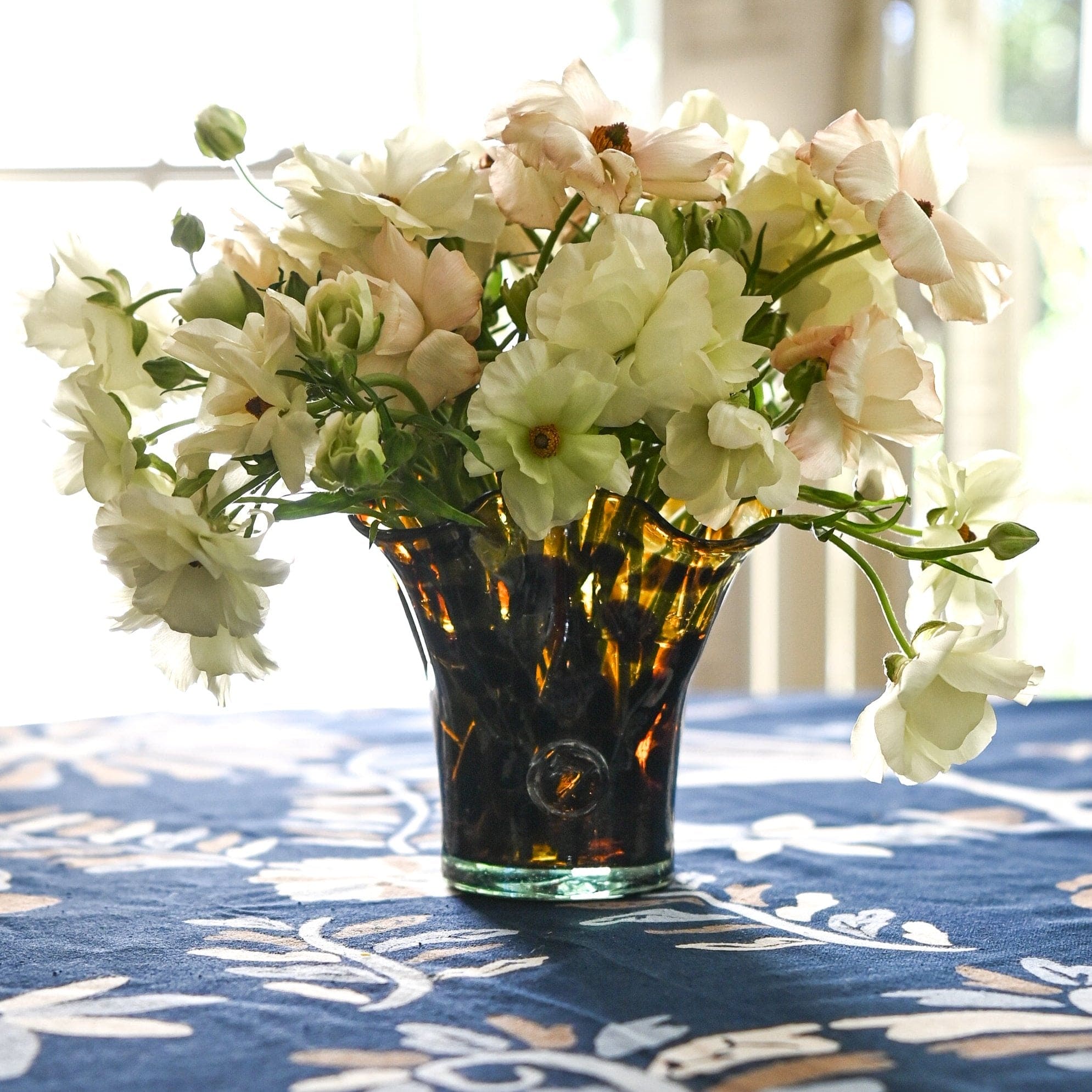 A petite lettuce leaf vase with a brown tortoise pattern containing flowers, placed on a table with a blue floral tablecloth.