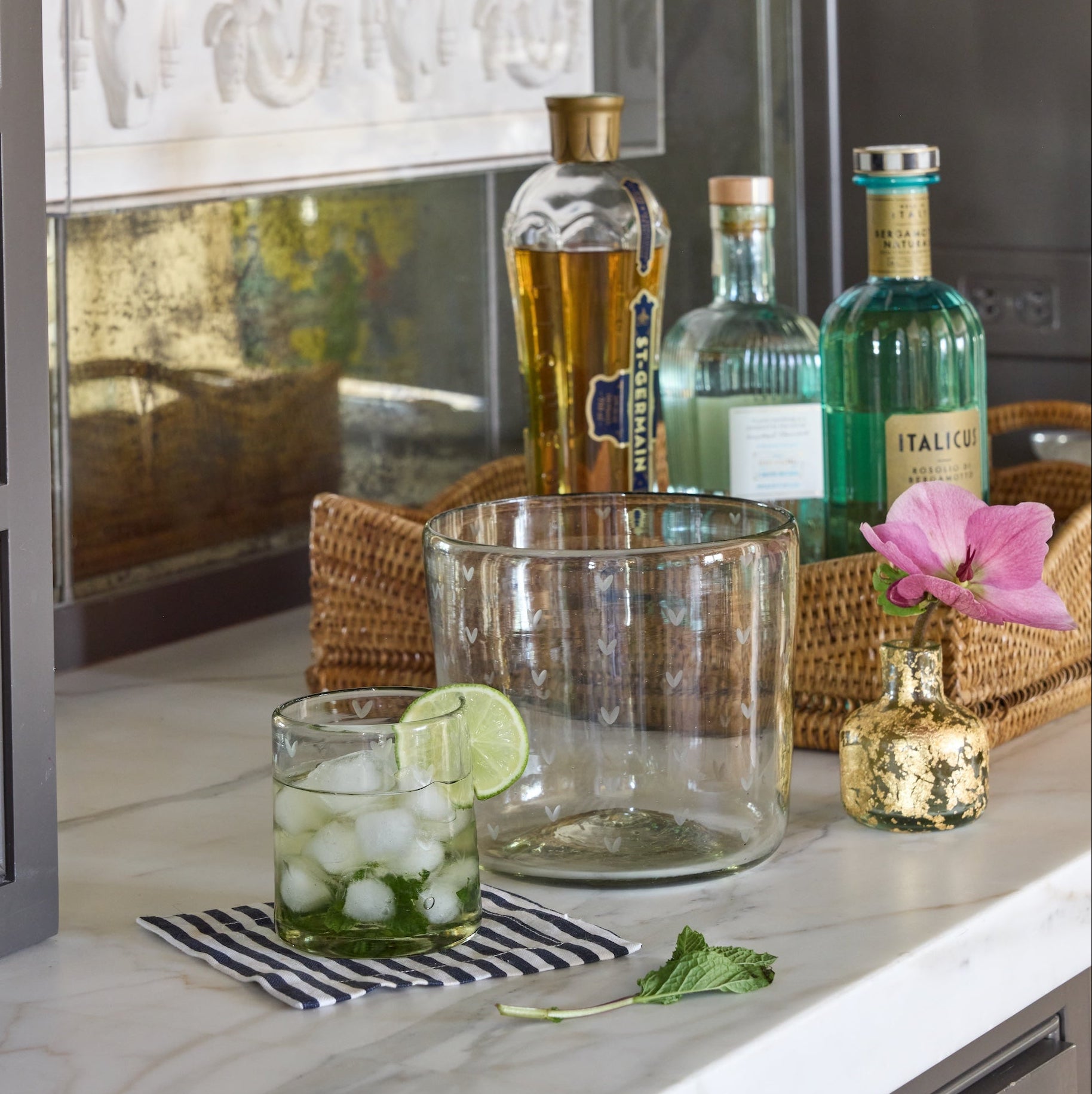 Alcohol bottles, glass vase with 14k gold leaf design and glasses on a kitchen counter with a decorative touch.