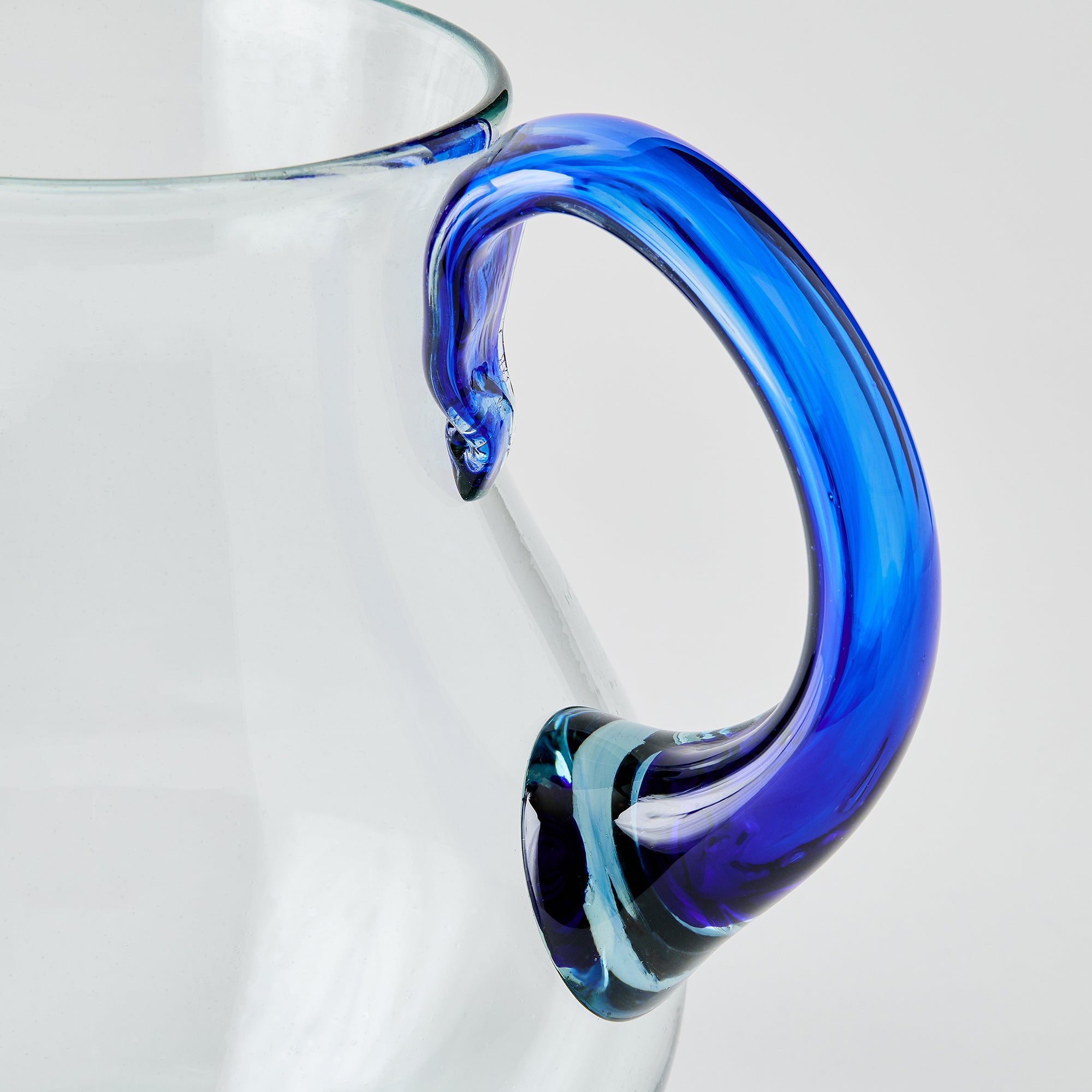 Clear glass pitcher with a blue handle on a light gray background