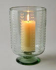 Decorative glass candle holder with a lit candle on a plain background