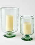 Two clear glass candle holders with white candles on a white background