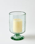 Clear glass candle holder with a white candle on a light gray background