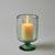 Green glass candle holder with a lit candle on a gray background
