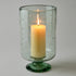 Candle in a green glass holder with star patterns on a gray background
