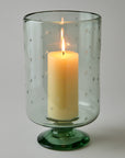 Candle in a green glass holder with star patterns on a gray background