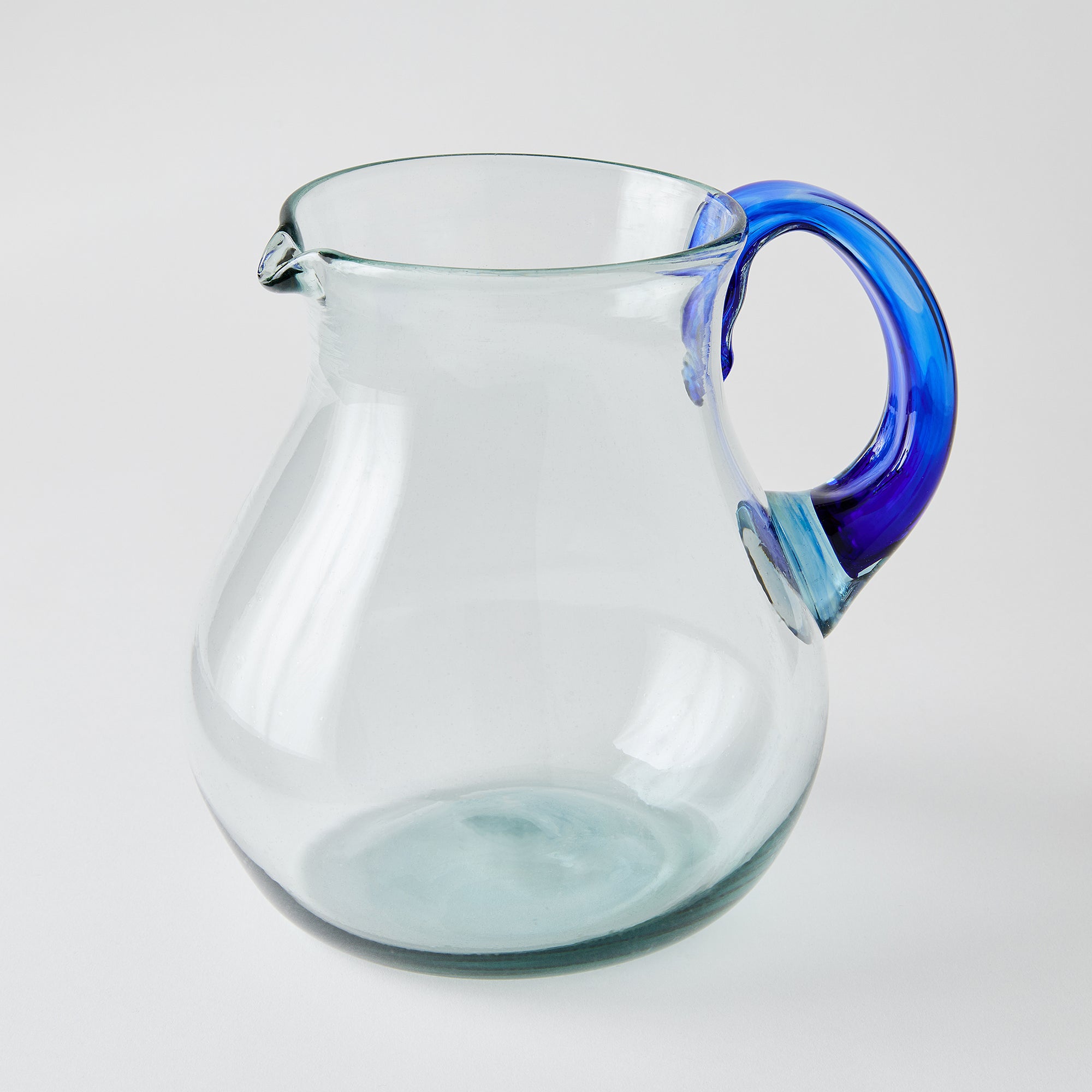 Clear glass pitcher with a blue handle on a white background