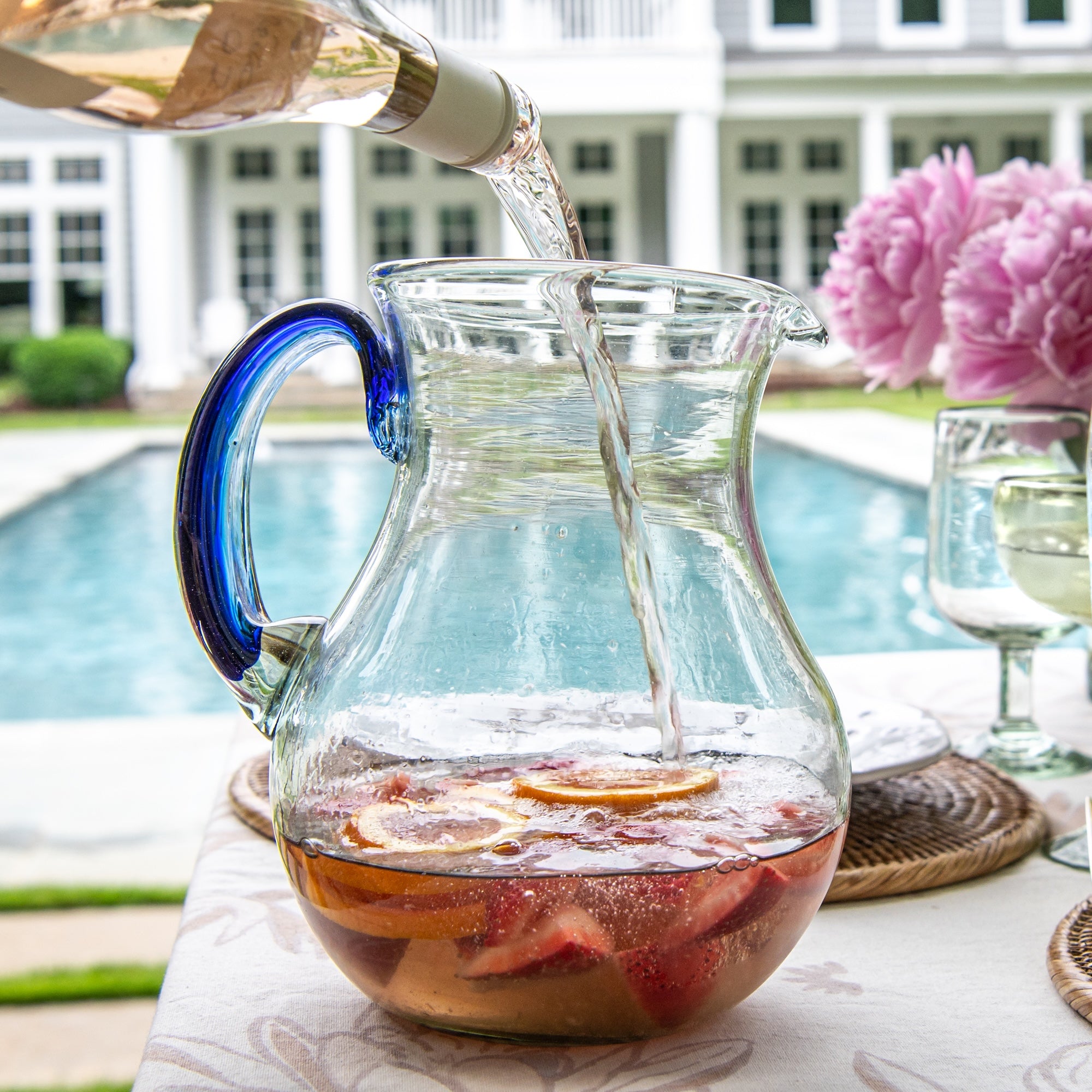 Glass pitcher with blue handle being filled outdoors by a poolside