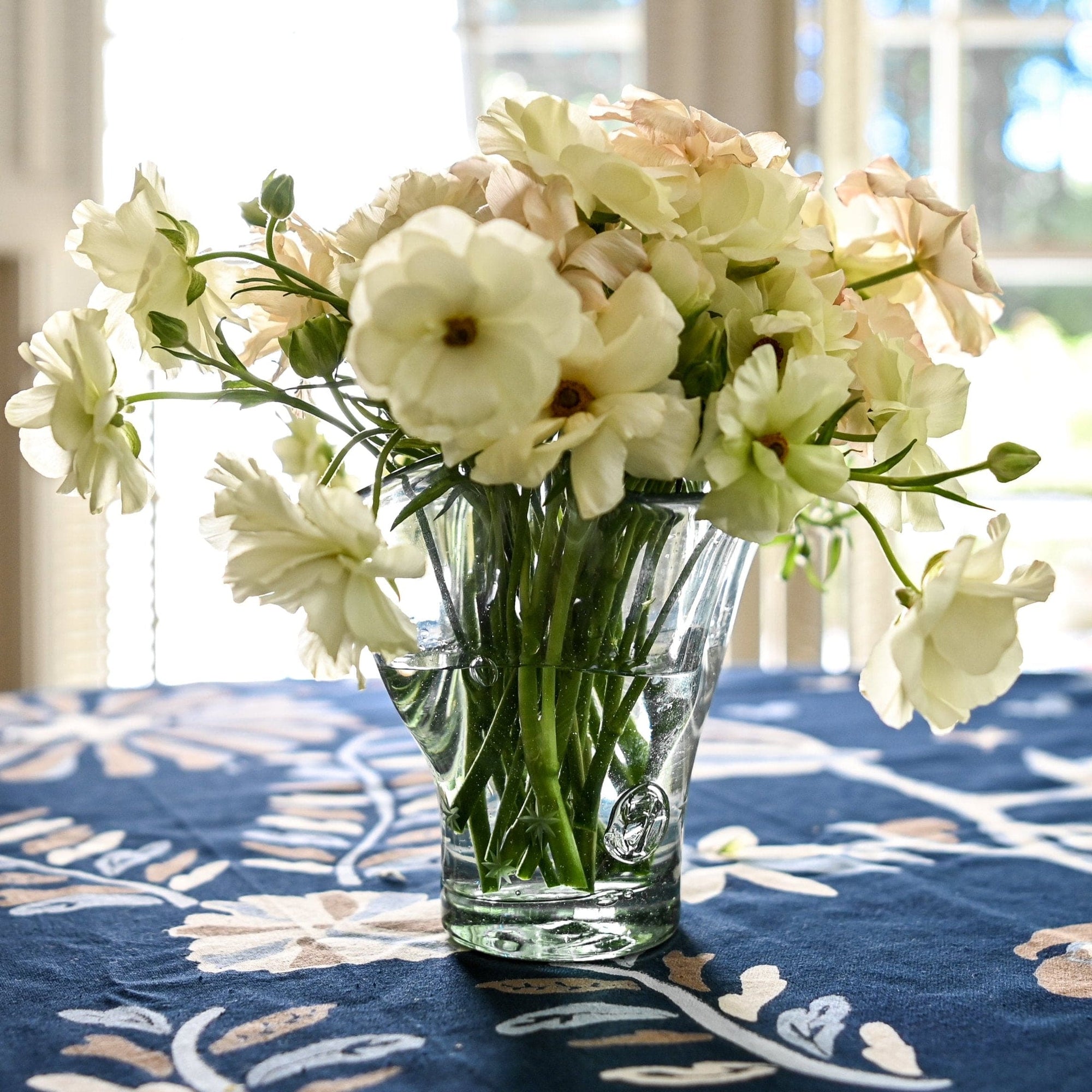 A clear glass vase with a starry base design, containing a bouquet of flowers, placed on a table with a blue floral tablecloth.