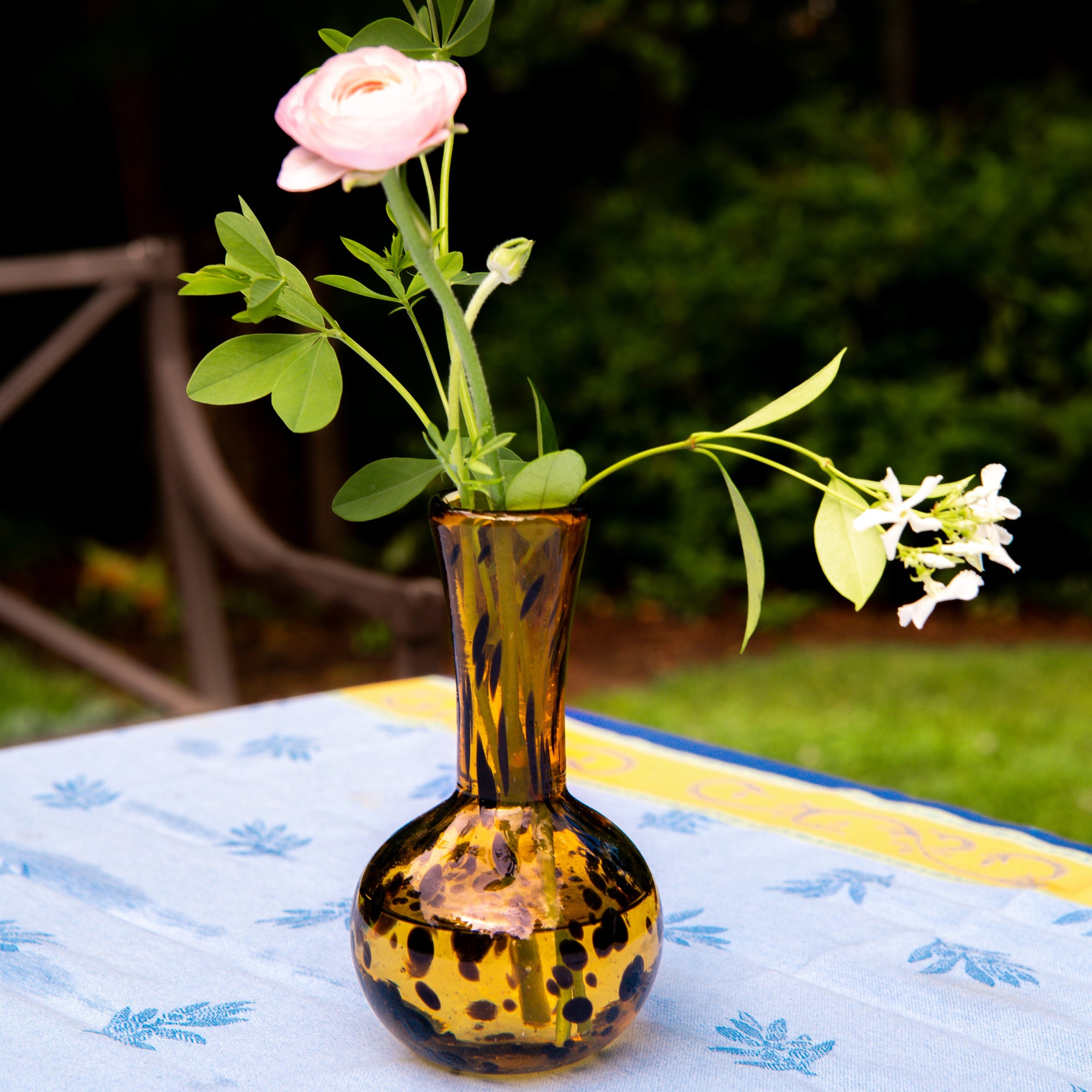Small amber glass vase with flowers on a table outdoors