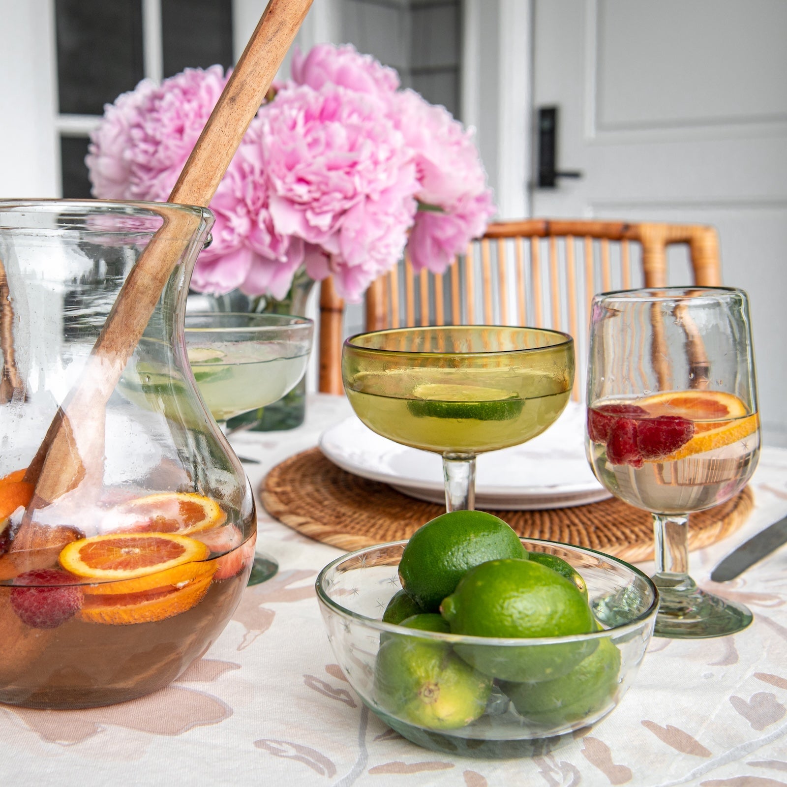 Table setting with a pitcher of sangria, glasses, and a bowl of limes and oranges.