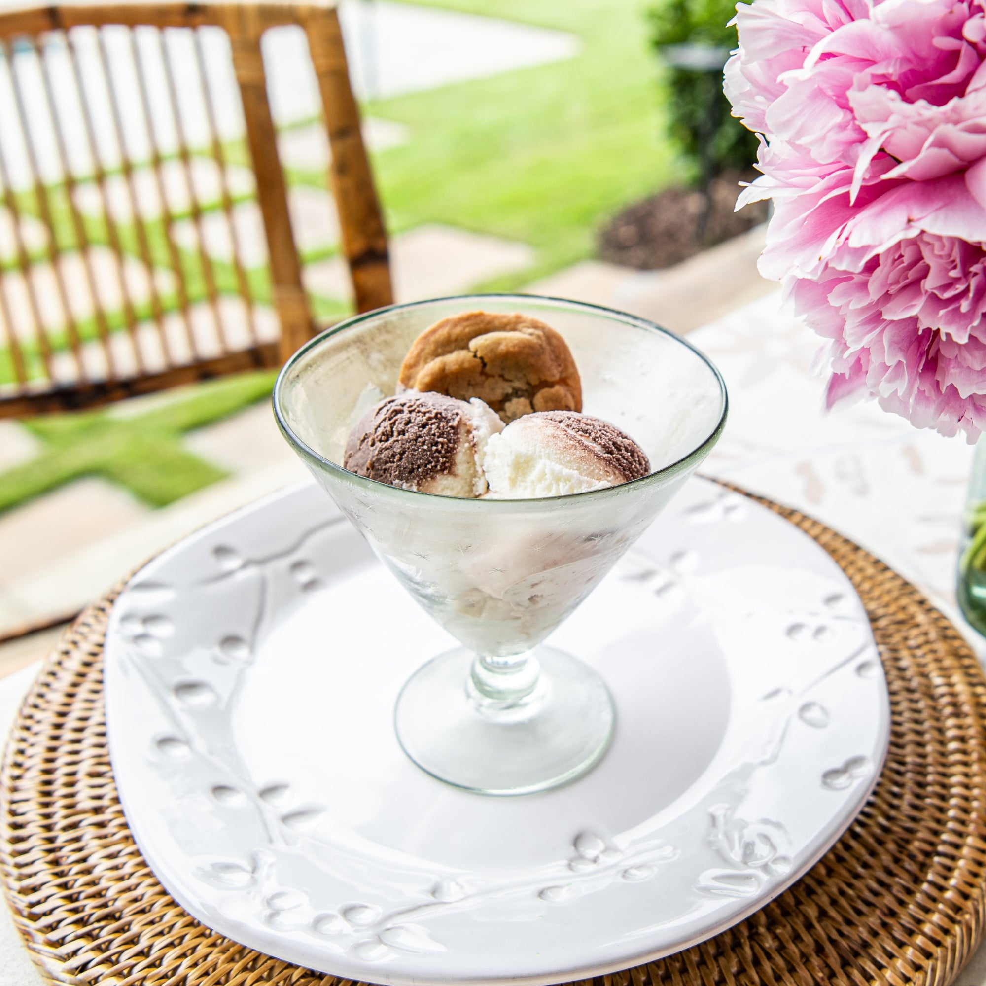 Ice cream dessert in a glass bowl on a white plate with pink flowers in the background