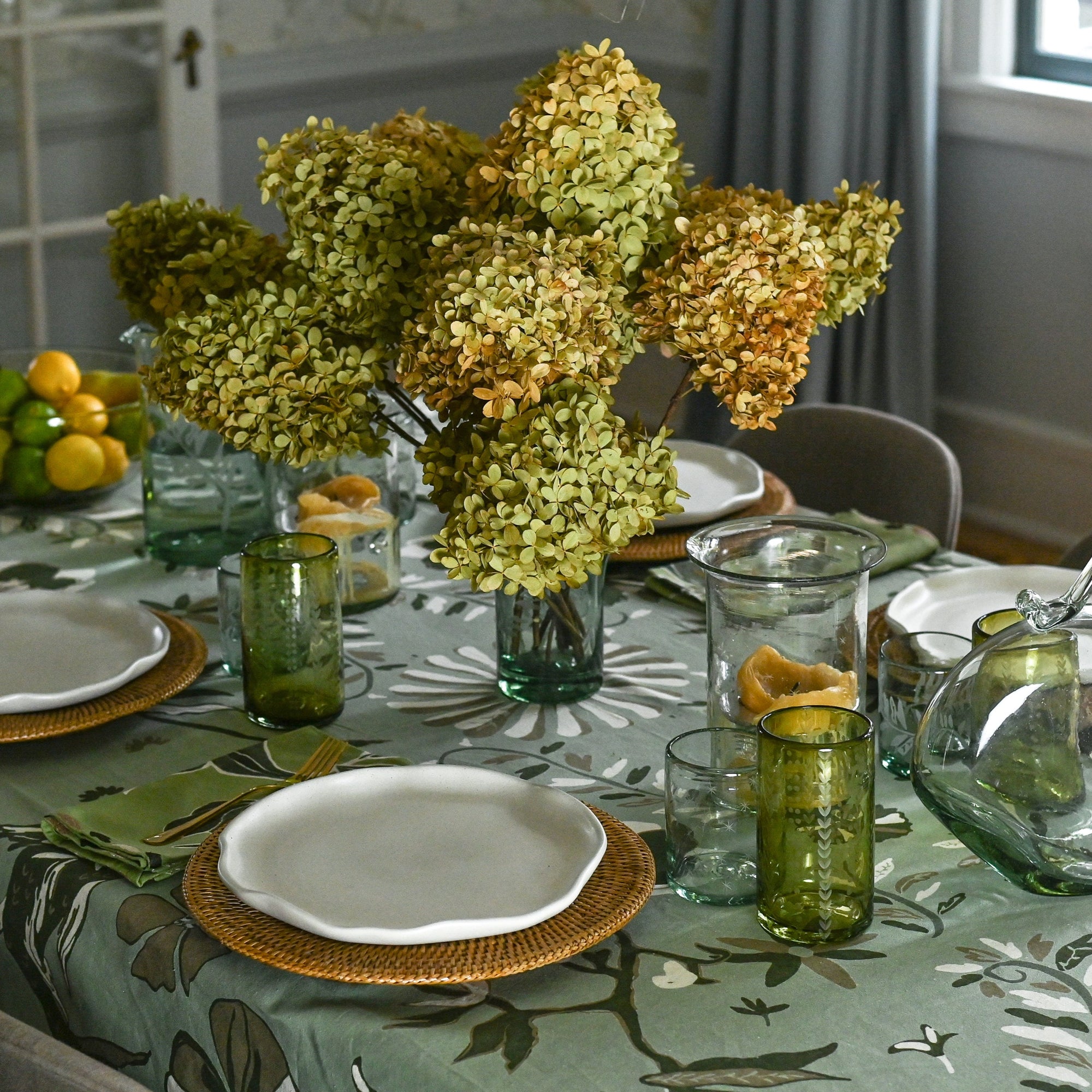 Dining table set with floral centerpiece, plates, and glasses in a room with curtains and a window.