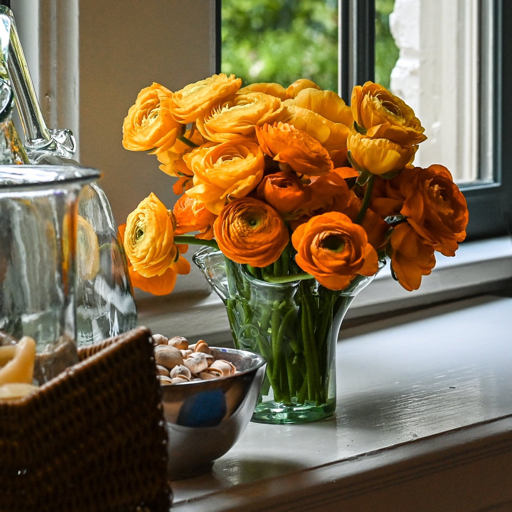 A clear glass vase with a fern motif, containing orange and yellow flowers, placed on a surface.