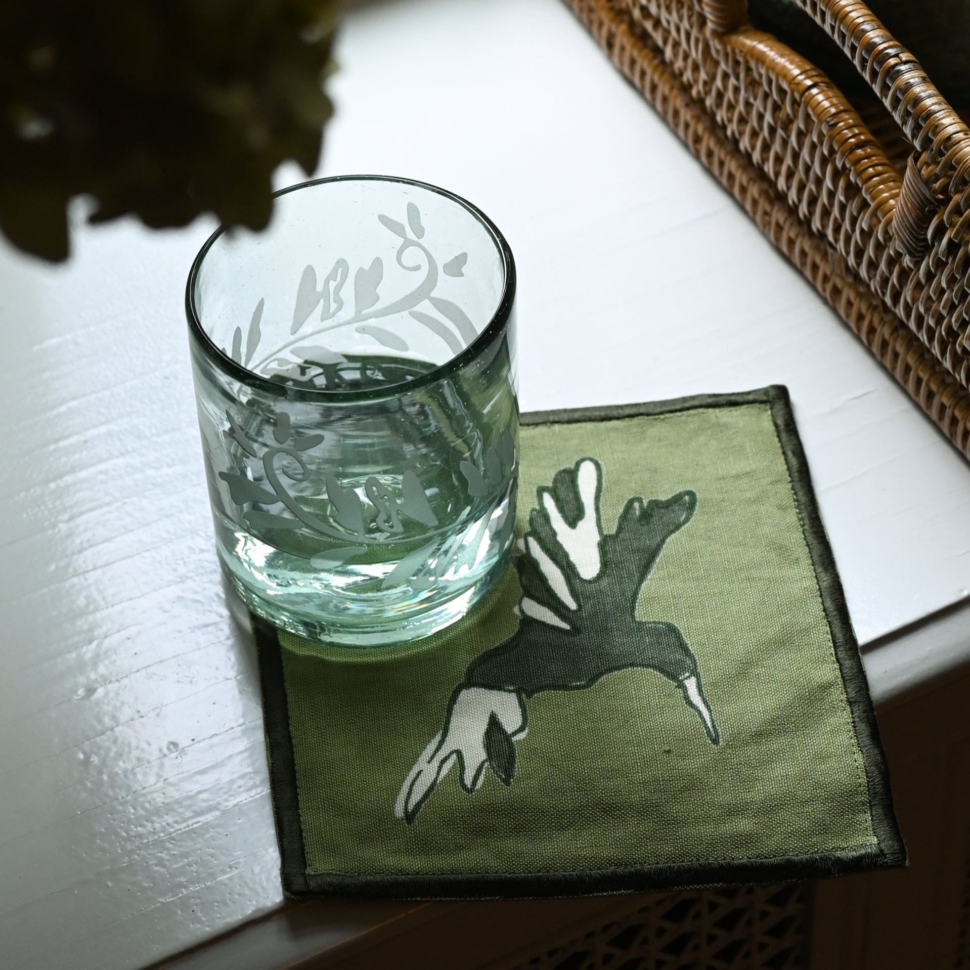 Clear glass with water on a green coaster with a deer design, placed on a white surface.