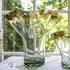 A clear glass vase with gold leaf ribbon rim, displayed in front of a window with a green outdoor background.