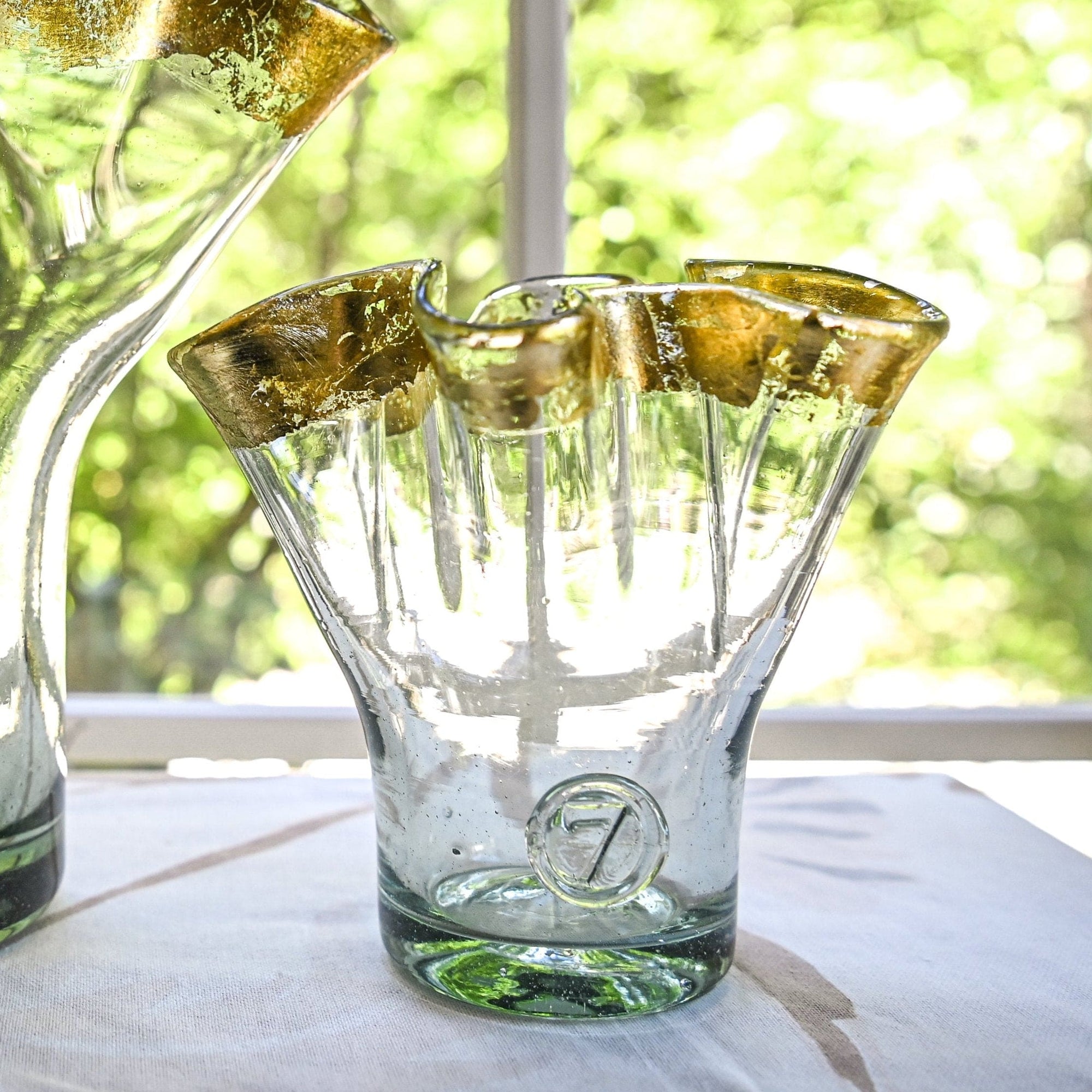 A clear glass vase with gold ribbon rim, placed on a table with a bright background, showcasing its unique shape and reflective gold detailing.