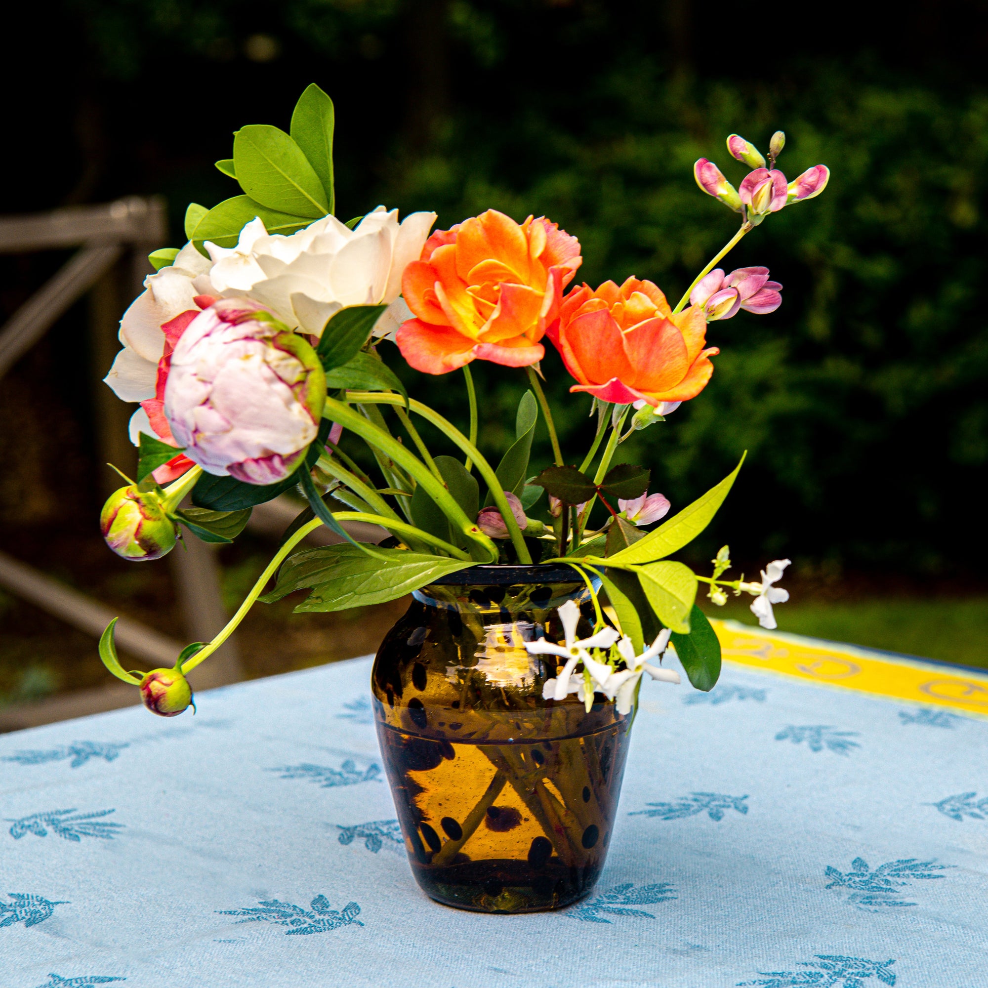 Vase with colorful flowers on a tablecloth outdoors