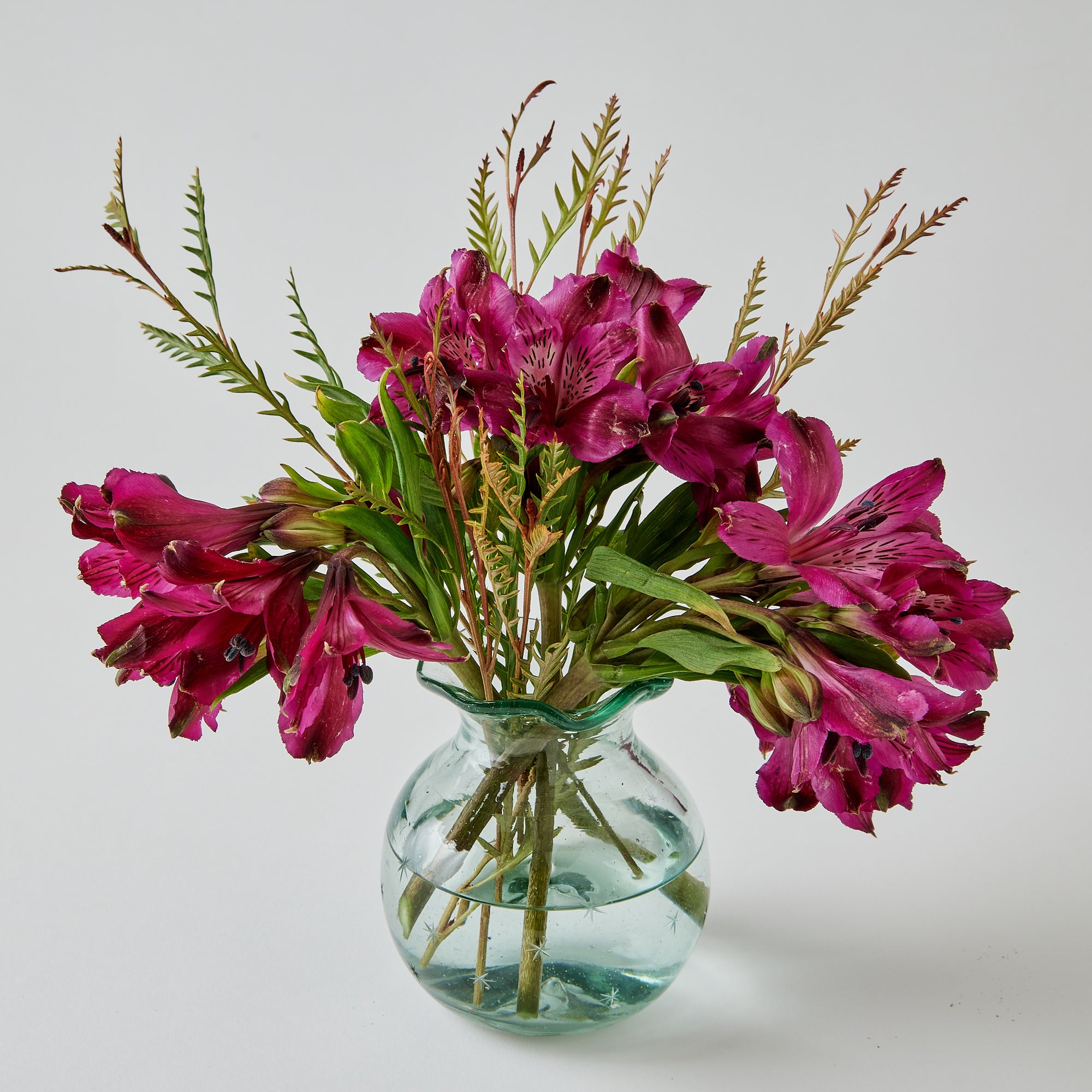 Clear starry glass vase with pink flowers on a light gray background