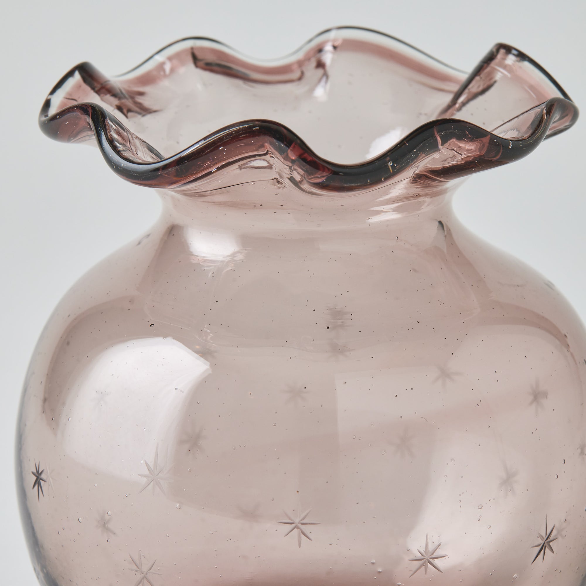 Pink glass vase with textured surface and wavy rim on a light background