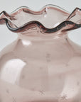 Pink glass vase with textured surface and wavy rim on a light background
