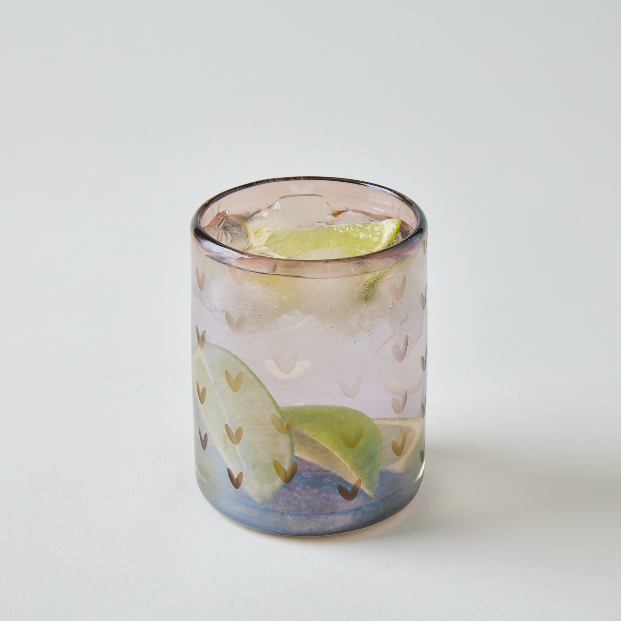 Glass with a drink, lime wedge, and ice cubes on a light gray background