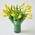 Green vase with yellow tulips on a white background