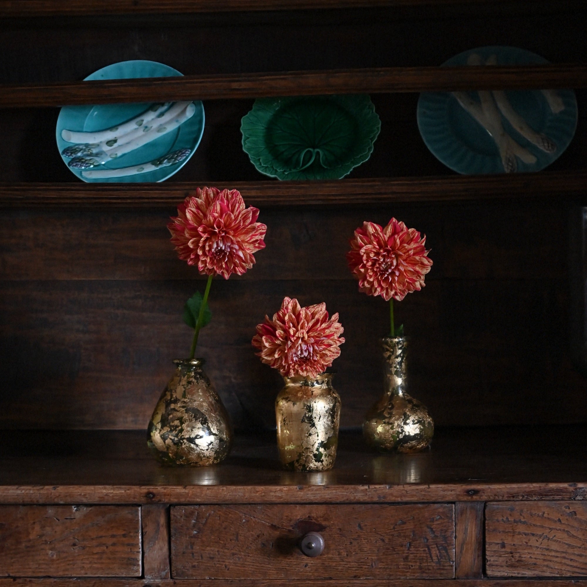Decorative setting with flowers in gold vases on a wooden surface, with teal plates in the background.