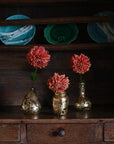 Decorative setting with flowers in gold vases on a wooden surface, with teal plates in the background.